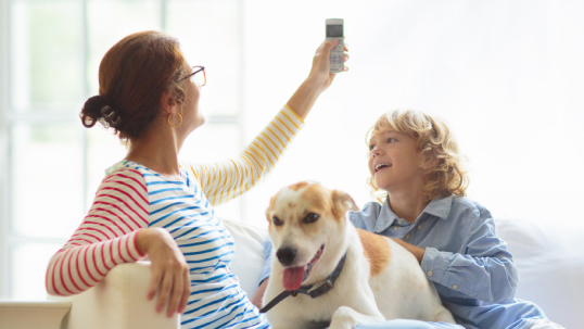 Woman sitting with her child and dog holding an air conditioning remote