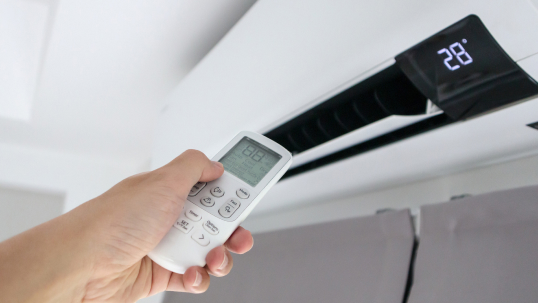 Person pointing a remote at their wall mounted air conditioner to adjust the temperature