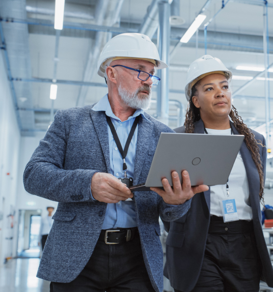 Man and woman inspecting a facility with hard hats and a laptop