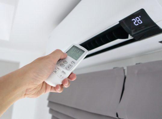 Person pointing a remote at a wall mounted air conditioner to adjust the temperature