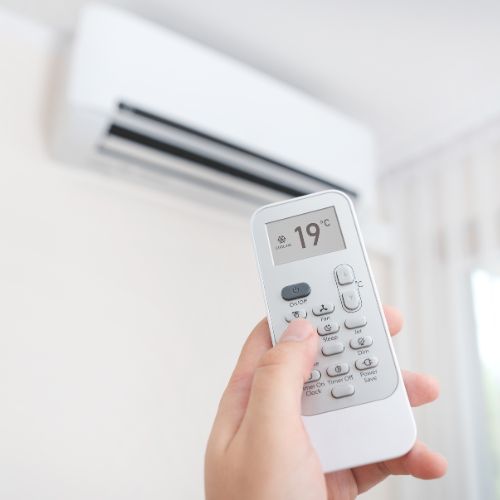 Person with a remote changing the temperature of a wall mounted air conditioner